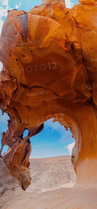 Captivating image of a natural rock arch showcasing vibrant, layered textures. The arch opens up to reveal a clear sky, embodying the beauty of erosion over time in Fuerteventura, Spain