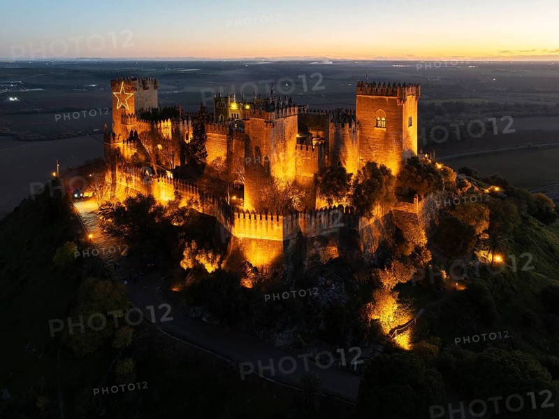 The impressive eighth-century Moorish castle of Almodóvar del Río perches high above the Guadalquivir river valley. Floodlit at dusk. Aerial view. Drone shot. Córdoba province, Andalusia, Spain