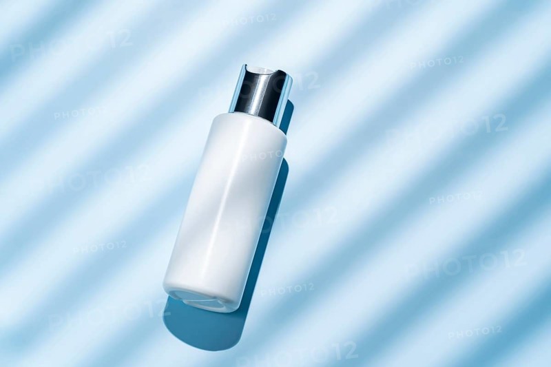 Top view of an elegant white cosmetic bottle on a vibrant blue background with soft diagonal light stripes, ideal for beauty and skincare marketing