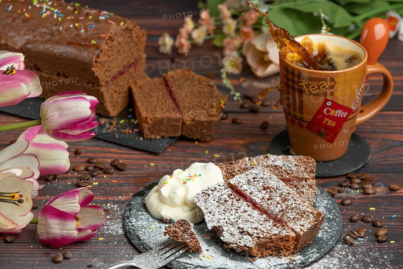 Cake with crumble and icing sugar next to whipped cream and cup with sparkling coffee, flower decoration