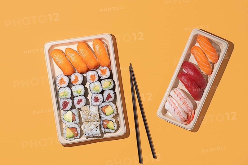 Minimalist overhead shot of sushi takeout boxes on a orange background, featuring nigiri and maki rolls with strong directional lighting