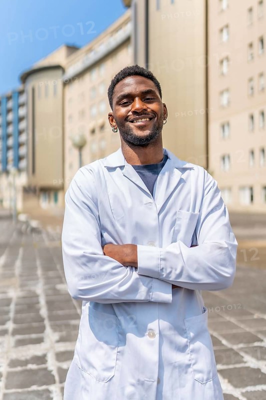 Vertical portrait of a smiling african doctor standing with arms crossed outside the hospital