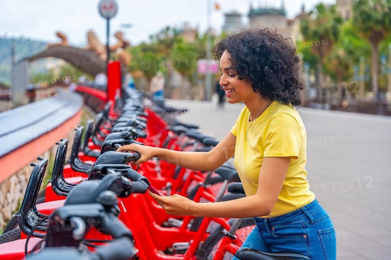 Side view of a latin young smiling woman using bike public sharing system in the city