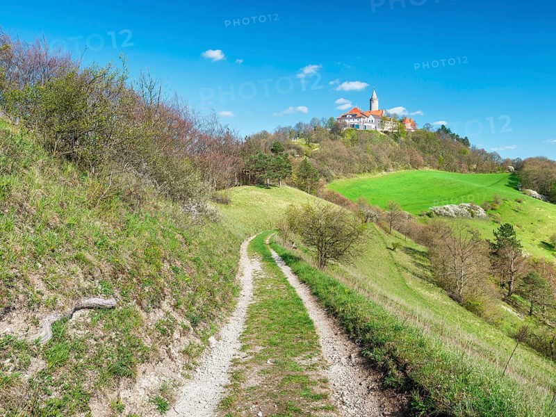 View of hilly landscape with green meadows and forests in spring, hiking trail leads to Leuchtenburg, Seitenroda near Kahla, Thuringia, Germany