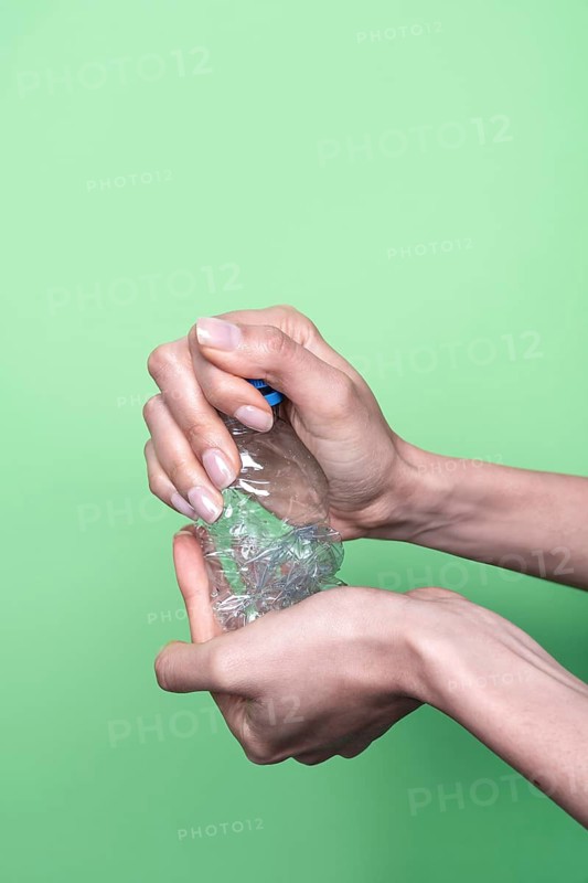 Two hands squeeze a clear plastic bottle, demonstrating recycling and waste reduction. The vibrant green background highlights the environmental focus on responsible plastic use