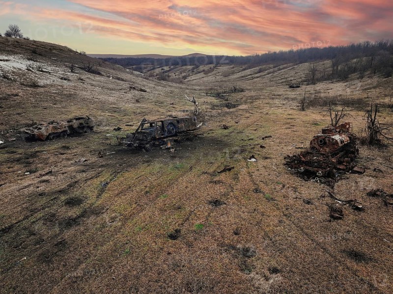 An aerial view showcases the devastating impact of war in a bleak Ukrainian landscape. Burnt out military vehicles litter a barren field, under a dramatic sunset sky