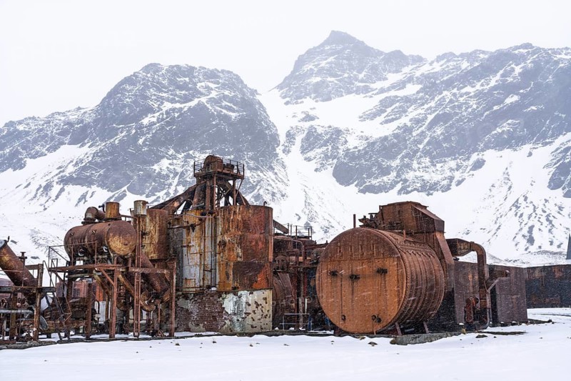 Rusted tanks and machinery at the abandoned whaling station, in front of snow-covered mountain peaks during snowfall, Grytviken, South Georgia