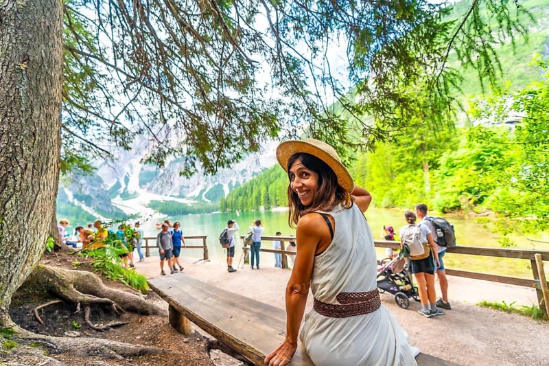 Woman wearing a straw hat sitting on a wooden bench, admiring the stunning landscape of lake braies in the italian dolomites during summer