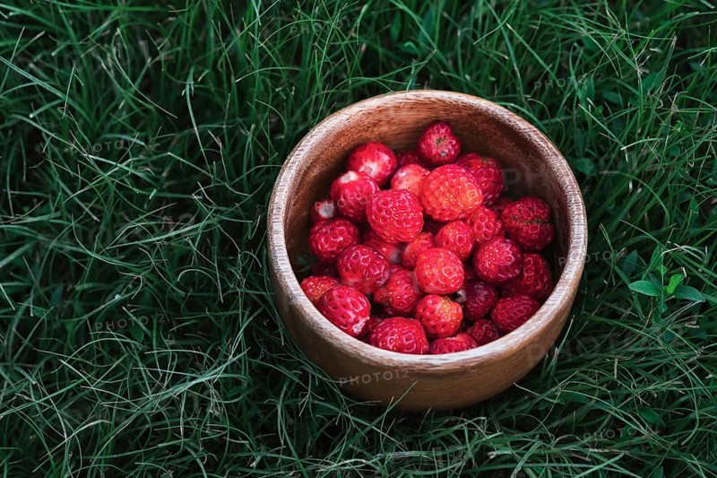 A wooden bowl filled with ripe red strawberries placed on lush green grass, capturing the essence of a fresh, natural, and healthy snack in an outdoor setting