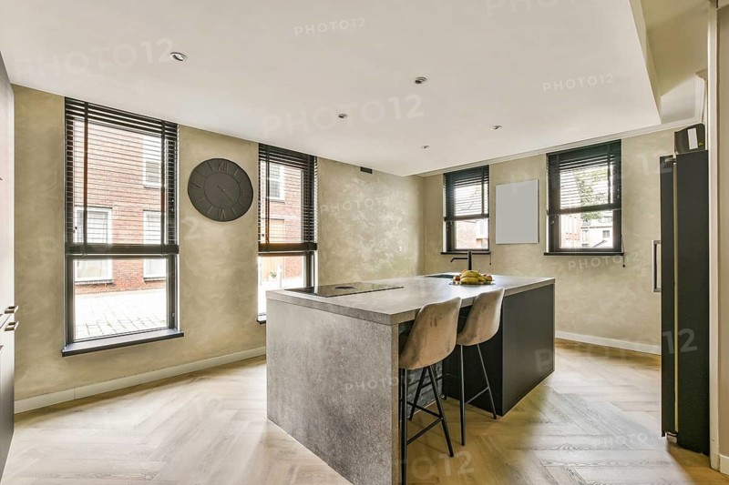 A stylish modern kitchen featuring sleek cabinetry, elegant bar stools, and ample natural light pouring in through large windows
