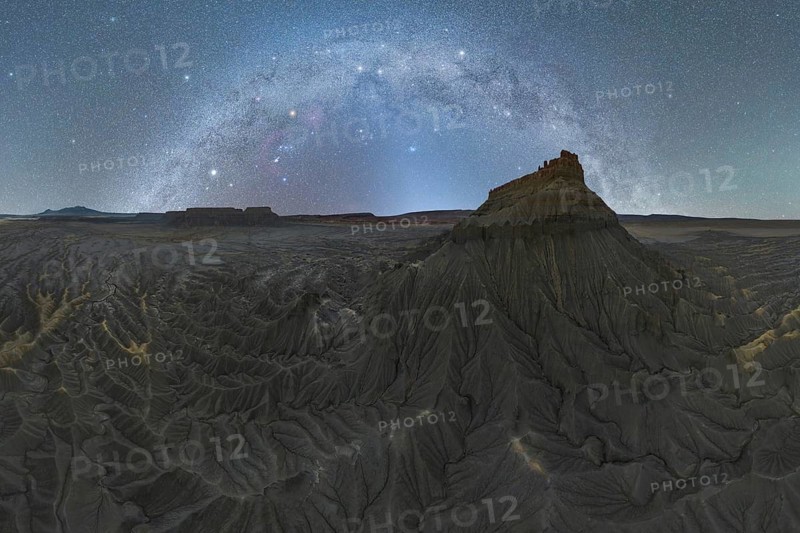 A breathtaking milky way arches over the rugged sandstone formations in the Utah desert. The night sky illuminates the unique terrain, creating an awe inspiring natural scene