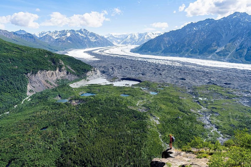 Young woman on a rocky outcrop enjoying the view, view of impressive mountain landscape with Matanuska glacier and glaciated mountain peaks, Lion's Head, Chugach Mountains, Alaska, USA