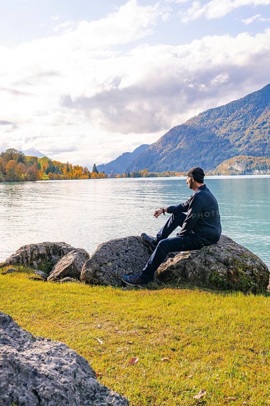 Man sitting on rocks on the lakeshore and enjoying the peaceful mountain landscape, Lake Brienz, Switzerland