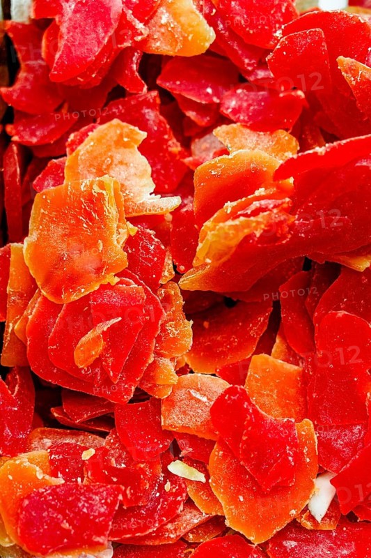 Close up of thinly sliced and vibrant dried papayas. The vivid red and orange hues create a striking contrast, emphasizing their natural sweetness and appeal