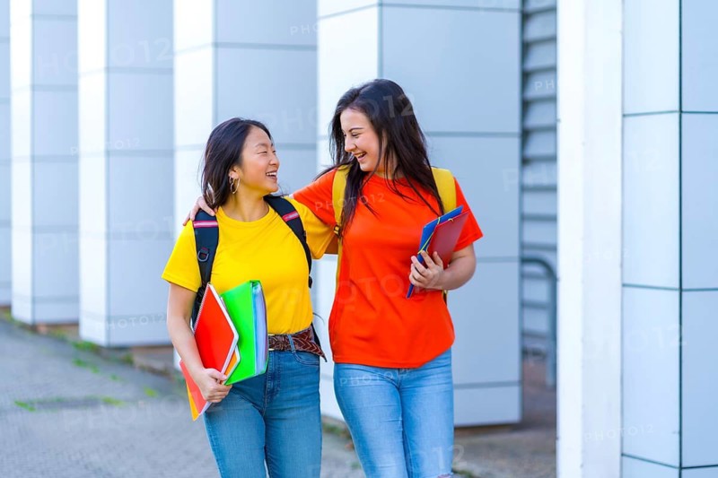 Multi-ethnic students embracing while walking to university in the street