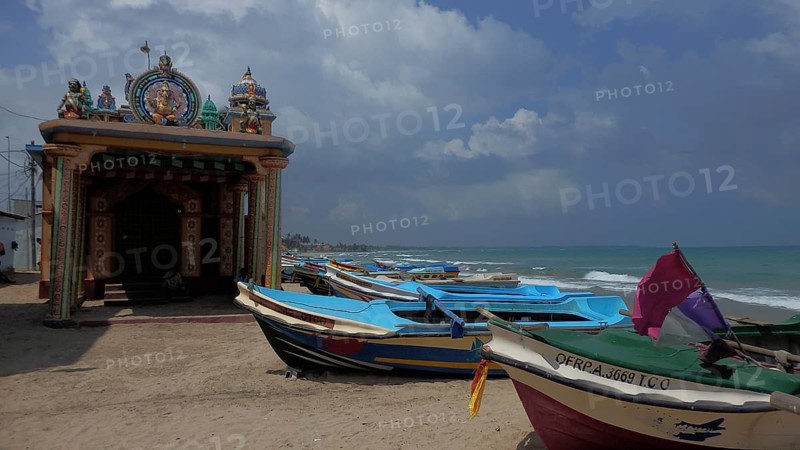 Several boats are moored on the beach next to an artfully designed Hindu temple, with calm sea in the background, Trincomalee, Sri Lanka