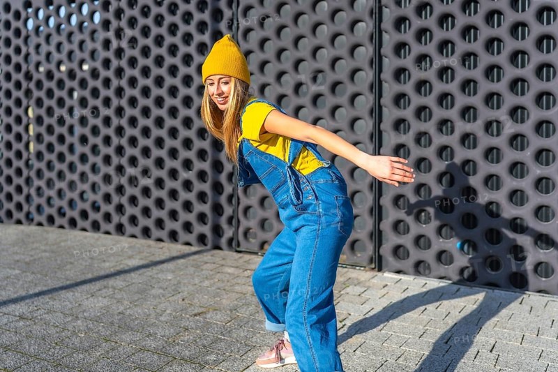 Young blonde woman dancing joyfully in casual clothes, expressing herself through urban dance outdoors under bright daylight in the city