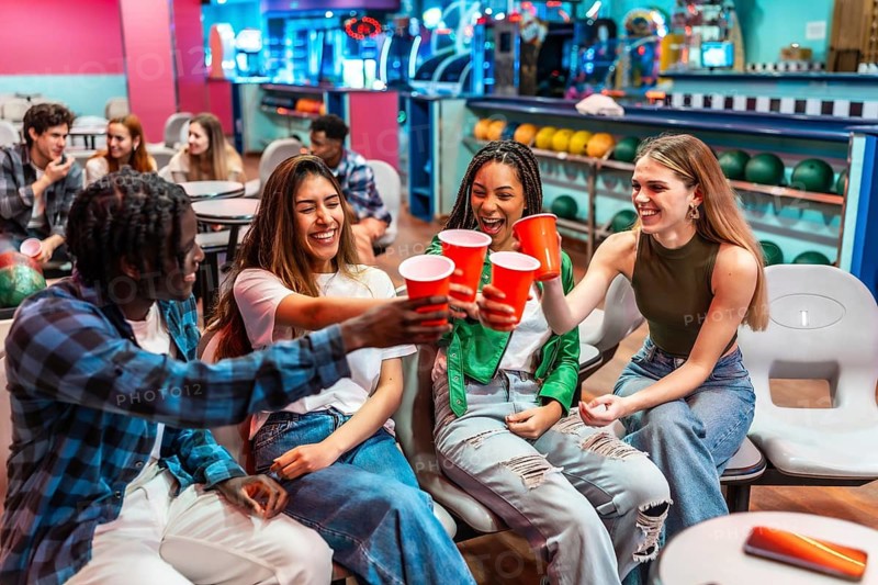 Group of cheerful young multiethnic friends toasting with red plastic cups while enjoying a fun weekend together at the bowling alley