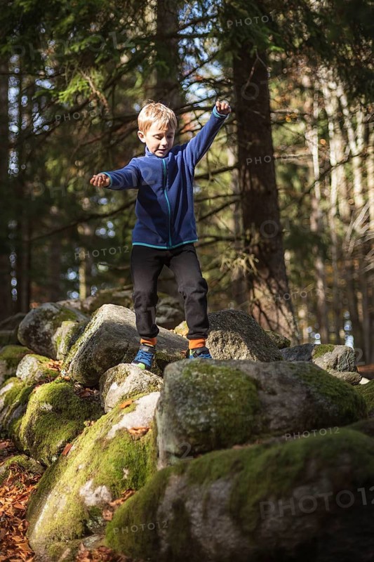 7 year old boy walks on rocks in the mountain forest