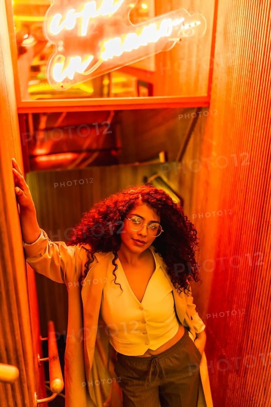 Vertical high angle view portrait of a latin woman in glasses against red neon sign looking at camera with confident expression