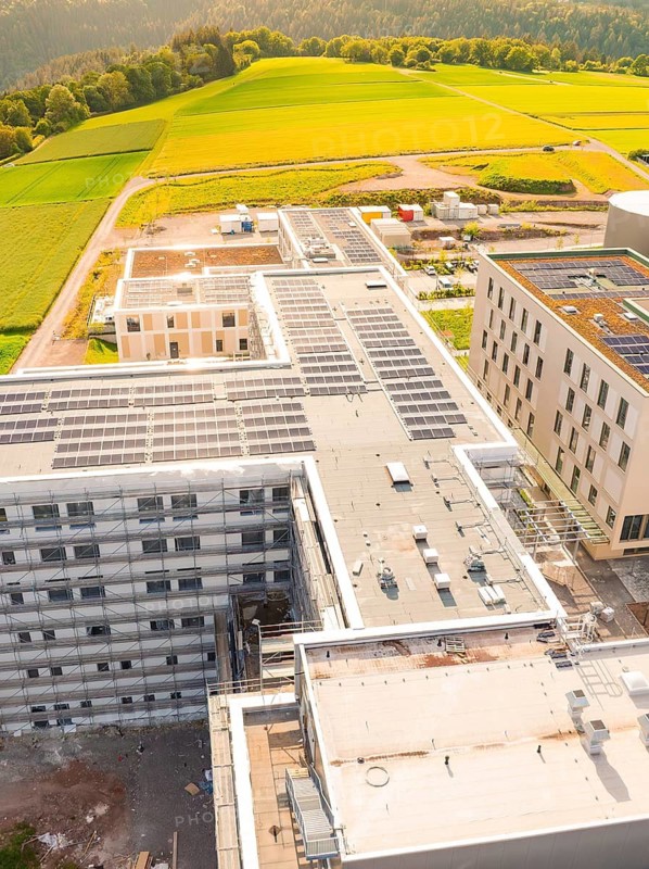 Roofs of a large building with solar panels, surrounded by green landscape, construction of the new hospital health campus Calw, Germany