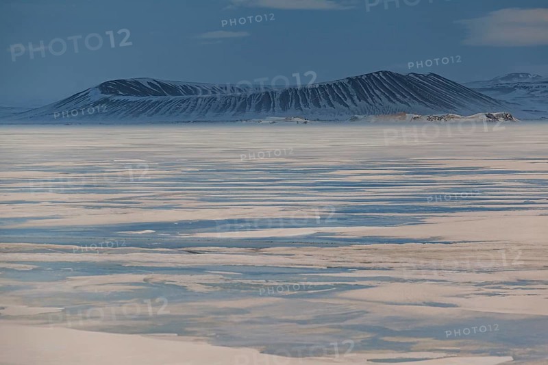 Frozen lake in a snowstorm, behind it Hverfjall crater, volcano, Myvatn, Iceland