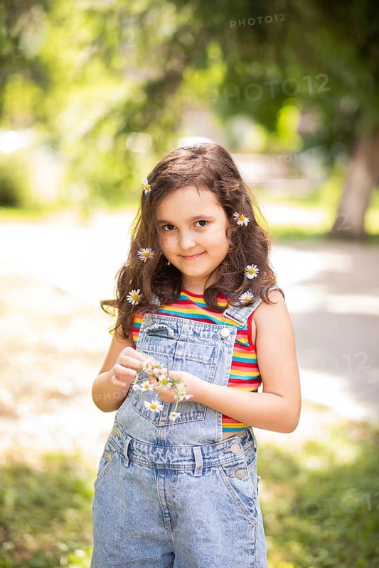 A joyful little girl smiling with chamomile flowers in her hair, enjoying the sunny outdoors. Her playful expression captures the essence of carefree childhood and nature