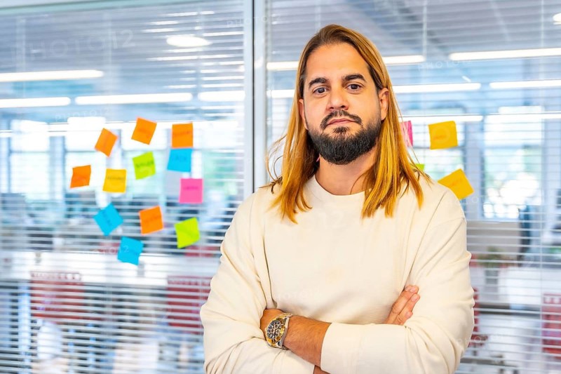 Portrait of a creative and young man standing with arms crossed next to a glass with adhesive notes in a coworking