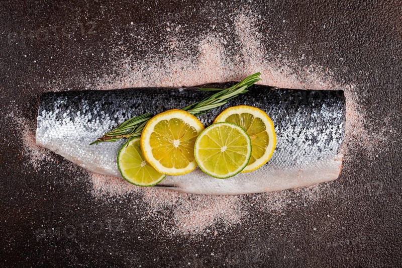 Fresh fish fillet, garnished with lemon and herbs, on a dark background, ready to cook