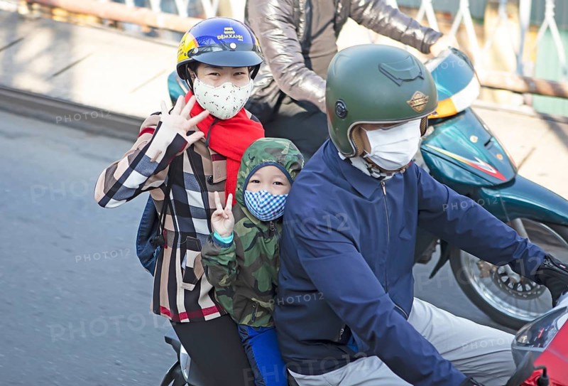 Vietnamese woman and child riding a moped over the Long Bien Bridge and waving at the camera, Hanoi, Vietnam