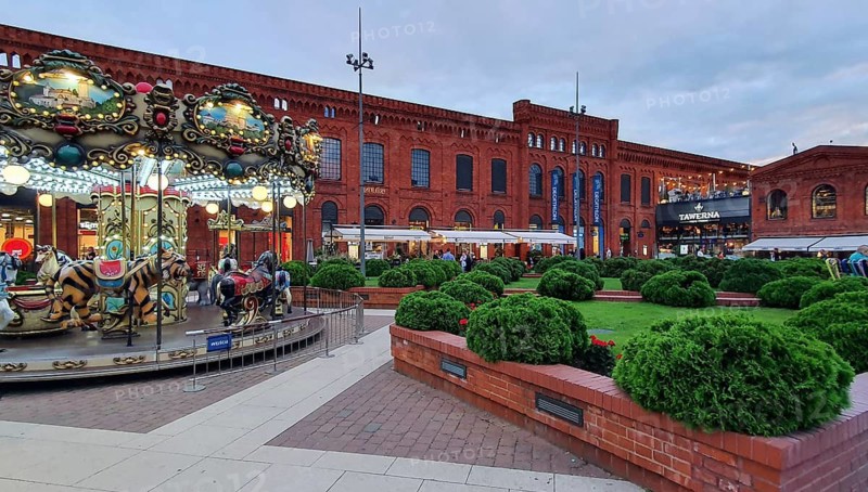 Amusement carousel and red brick façade with manicured bushes at dusk, Manufaktura, Lódz, Lodz, Lodz, Poland