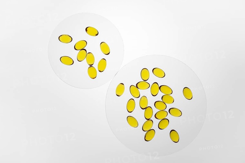 Bright yellow omega-3 and vitamin D capsules displayed on two white surfaces, highlighting their colorful and glossy appearance, ideal for health and wellness themes