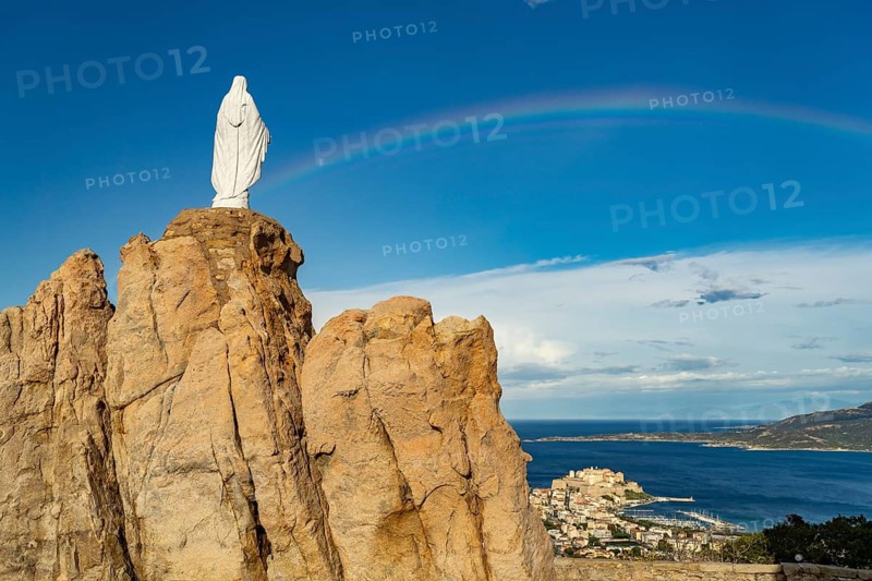 Rainbow on the statue of the Virgin Mary on a rock next to the Notre Dame de la Serra pilgrimage chapel in Calvi, Balagne, Corsica, France