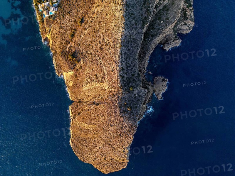 A stunning aerial view of the Costa Blanca coastline, where rugged cliffs meet the calm Mediterranean Sea at sunrise, creating a breathtaking and serene landscape