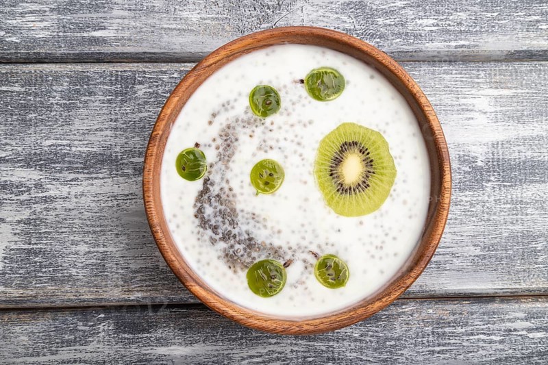 Yogurt with kiwi, gooseberry, chia and almonds in wooden bowl on gray wooden background. top view, flat lay, close up