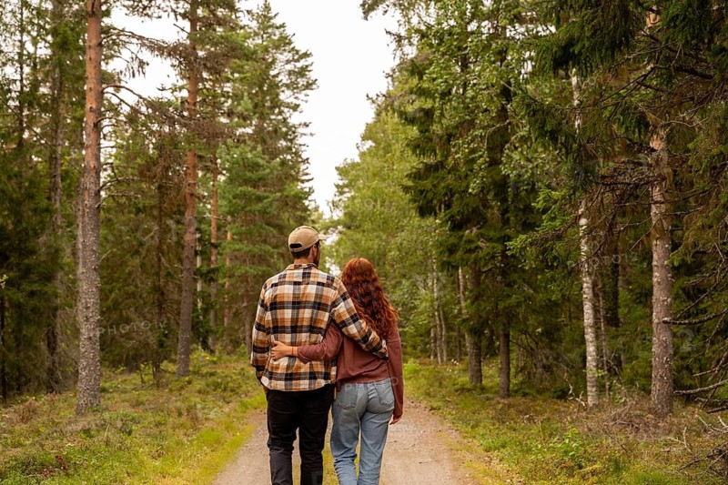 A couple embraces while walking through a lush green forest path in Sweden, surrounded by tall trees and natural beauty, symbolizing love and tranquility in nature