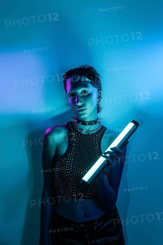 A striking cyberpunk-themed model poses under vibrant neon lights, holding a futuristic light stick. Her edgy style embodies a modern blend of technology and fashion