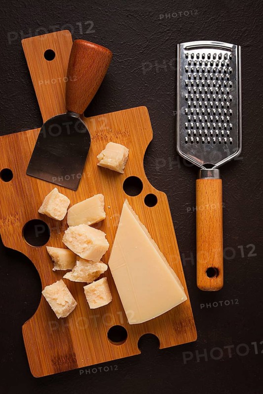 Hard cheese, parmesan, on a cutting board, cheese knife, grater, top view, no people