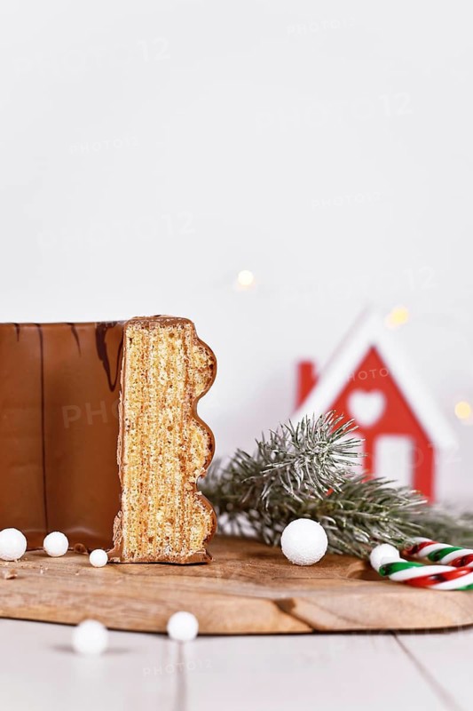 Cut open traditional German layered winter cake called 'Baumkuchen' glazed with chocolate, surrounded by seasonal decoration