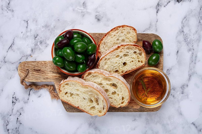 Appetizer, sliced ciabatta bread, with olive oil, green olives, Chalkidiki olives, classic Green green olive, on a marble table, top view, no people