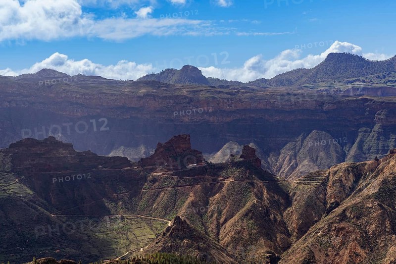 Expansive view showcasing the rugged terrain and serene beauty of Roque Bentayga in Artenara, Gran Canaria, with deep gorges and rolling peaks under a blue sky
