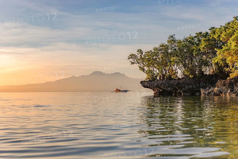 Sunrise illuminates a serene seascape in the Philippines with a boat nearby and mountains in the background, highlighting the tranquil beauty of a tropical vacation
