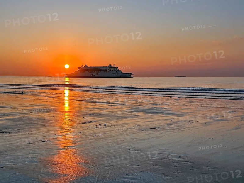 Sunset over the beach with a ship and a warm orange sky, Atlantic Ocean, Calais, France