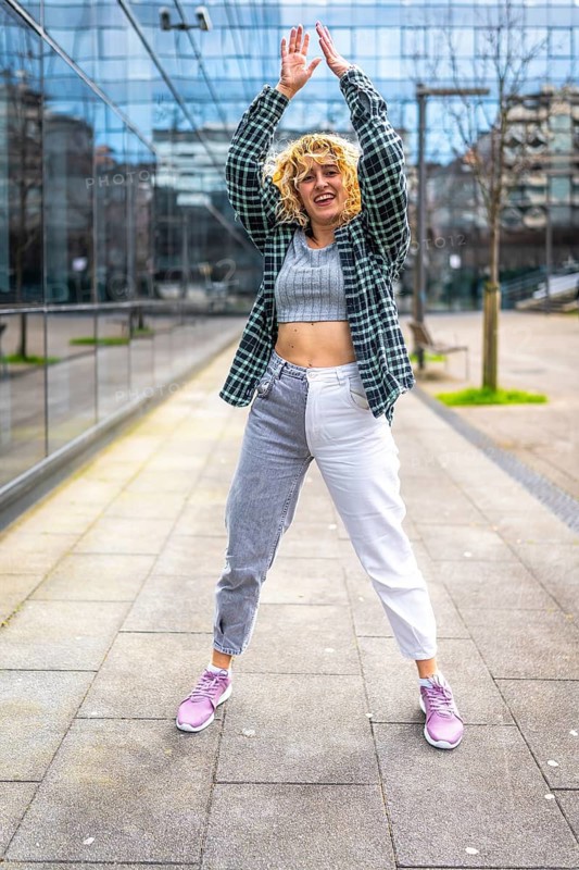 Young caucasian woman dancing modern urban music in the city with checkered shirt and two tone trousers
