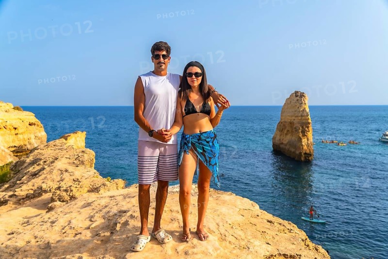 Tourists standing on a cliff enjoying the scenic view of the atlantic ocean and a sea stack near praia da marinha in algarve, portugal, during their summer holidays