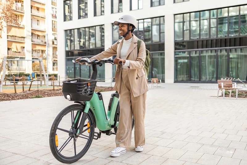 A stylish black woman in an urban setting, confidently riding a bicycle, surrounded by modern architecture She embodies a blend of fashion and mobility