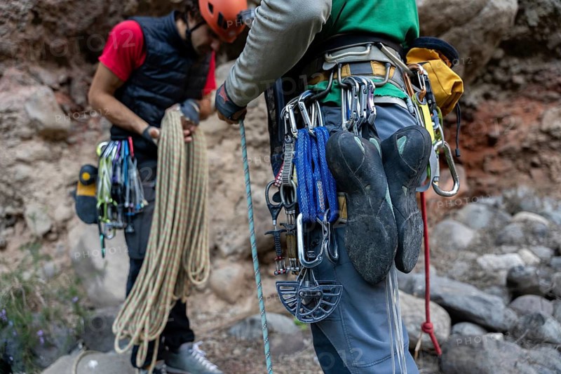 Climbers equipped with gear prepare for a traditional climbing adventure in natural surroundings. The image captures ropes, carabiners, and climbing shoes ready for use