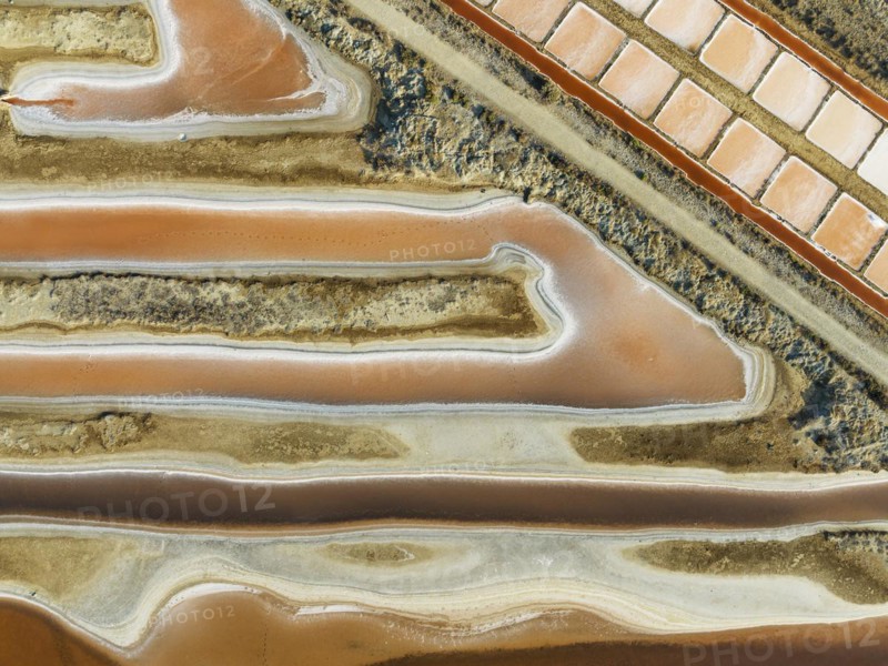 Saline ponds at the salt works near Chiclana de la Frontera. The orange-red colour depends on the level of salinity and is directly caused by the algae Dunaliella salina and brine shrimp. Aerial view. Drone shot. Cádiz province, Andalusia, Spain