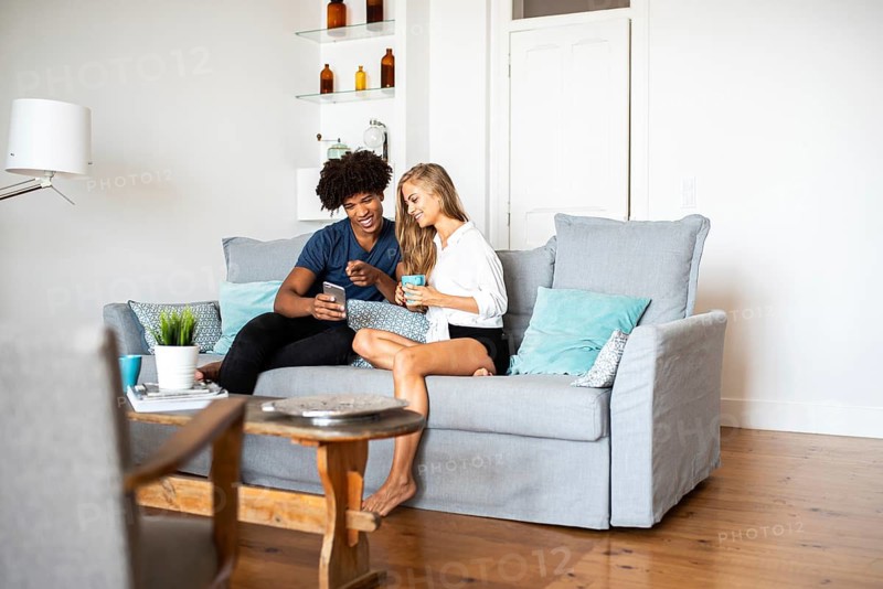 A joyful couple relaxing on a cozy sofa at home, chatting and sharing a moment of happiness. The living room features modern decor, creating a warm atmosphere