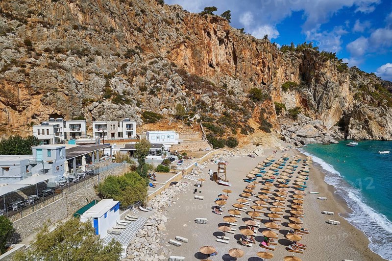 An aerial view of a beach with a building surrounded by steep rocks and many sunbeds and parasols, Kyra Panagia, Kyra Panagia Beach, East Coast, Karpathos, Dodecanese, Greek Islands, Greece
